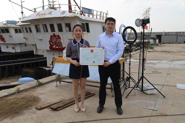 海鮮電商張夢琴與幫辦員手持食品經(jīng)營許可證合影。贛榆區(qū)委宣傳部供圖