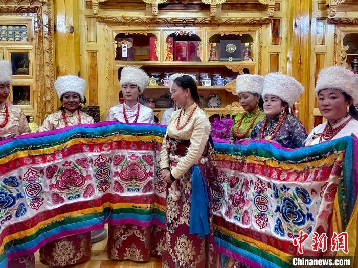 圖為女性展示村民自發(fā)繡制的“百米五彩哈達(dá)”?！±钣穹?攝